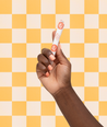Hand holding a small product against a yellow and white checkered background