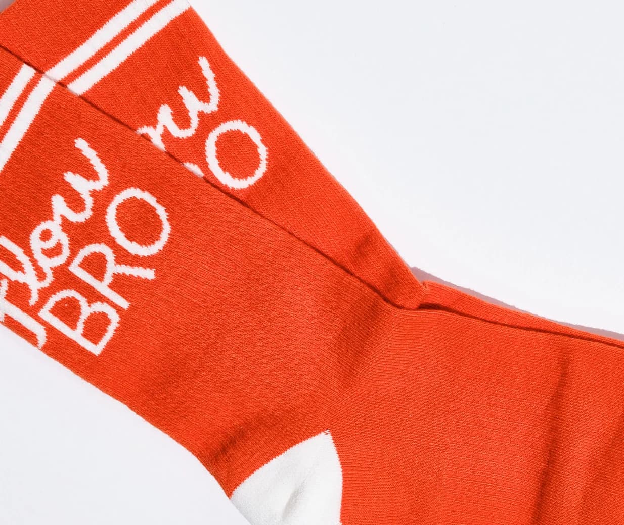 A close-up of a bright orange crew sock with white knit lettering that reads 'flow BRO' and white stripes near the cuff, shown on a plain white background.